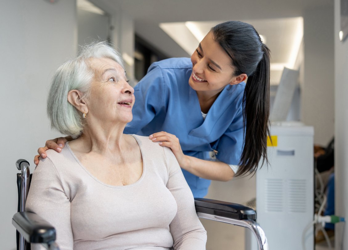 Aster Care Home Saskatoon Compassion-nurse talking to a old woman in whseelchare keeping her hand in old man's sholder in Aster Care Home Saskatoon-Saskatoon